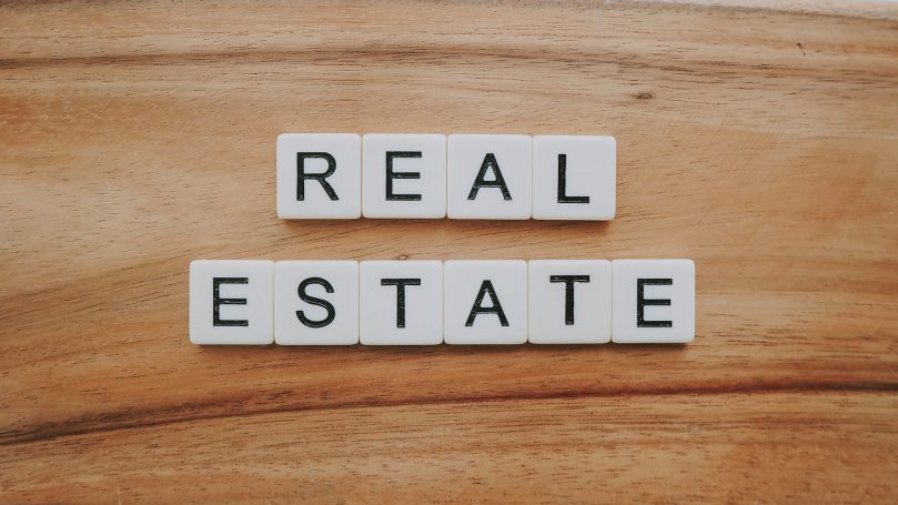Die Wörter "REAL ESTATE" in weißen Blockbuchstaben auf Holzuntergrund.